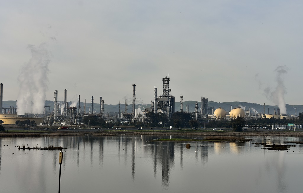 Martinez refinery with numerous smokestacks belching effluent against the coastal hills