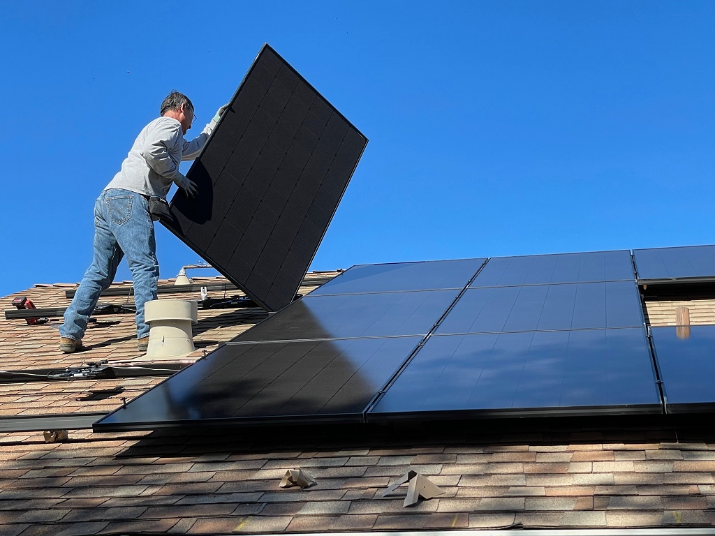 Man installing a solar panel on a shingled roof