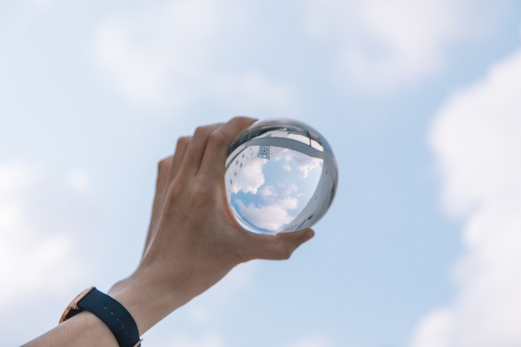 Hand holding glass globe against blue sky