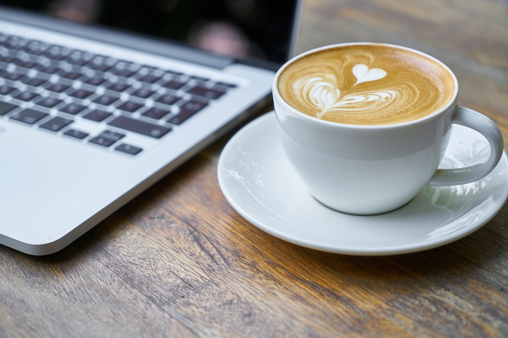 Laptop with latte in white cup and saucer with heart motif in the latte foam