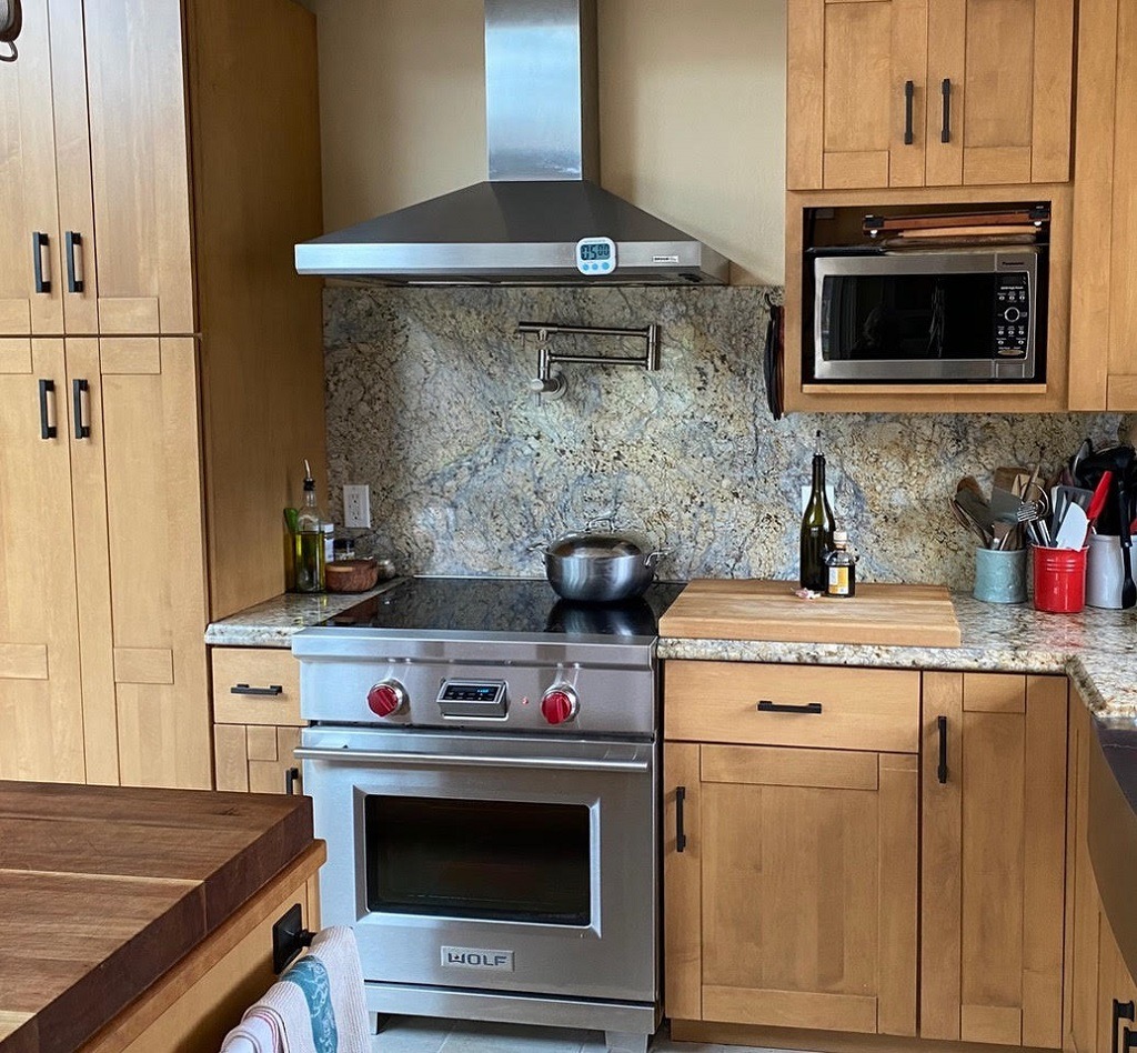 Partial kitchen scene with blond cabinetry, a stainless steel stove with a ceramic/glass cooktop, a microwave, and various kitchen utensils tidily resting on countertops