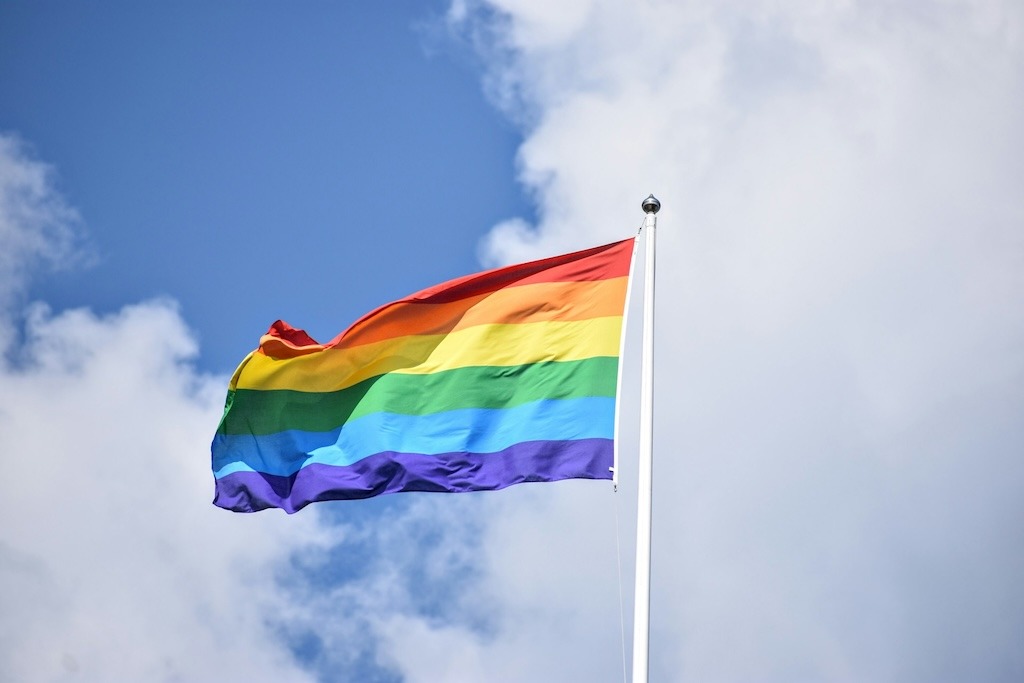 Pride flag unfurled over white clouds in a blue, blue sky | Image credit: Rob Maxwell on Unsplash